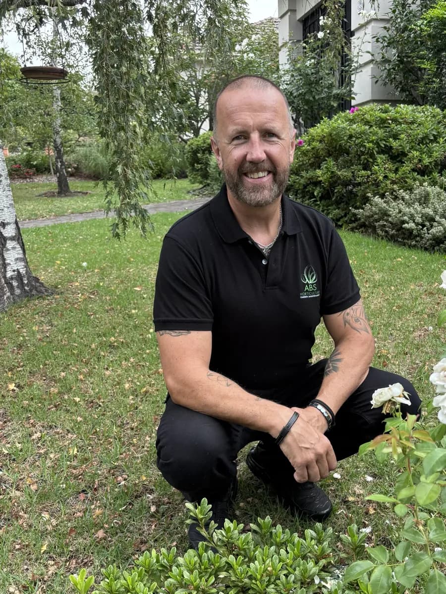 Anthony Bennett, founder of ABS Horticulture, crouching beside a garden bed in his ABS polo shirt